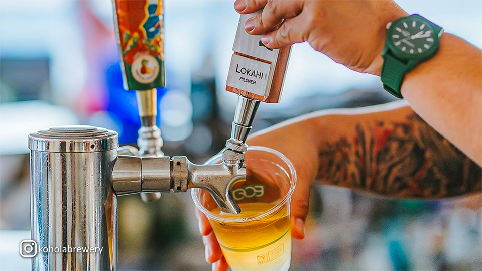 Lokahi Pilsner being poured into an Eco plastic cup at Kohola Brewery’s Tap Room in Wailea, Maui, showcasing the golden beer and tap faucet up close.