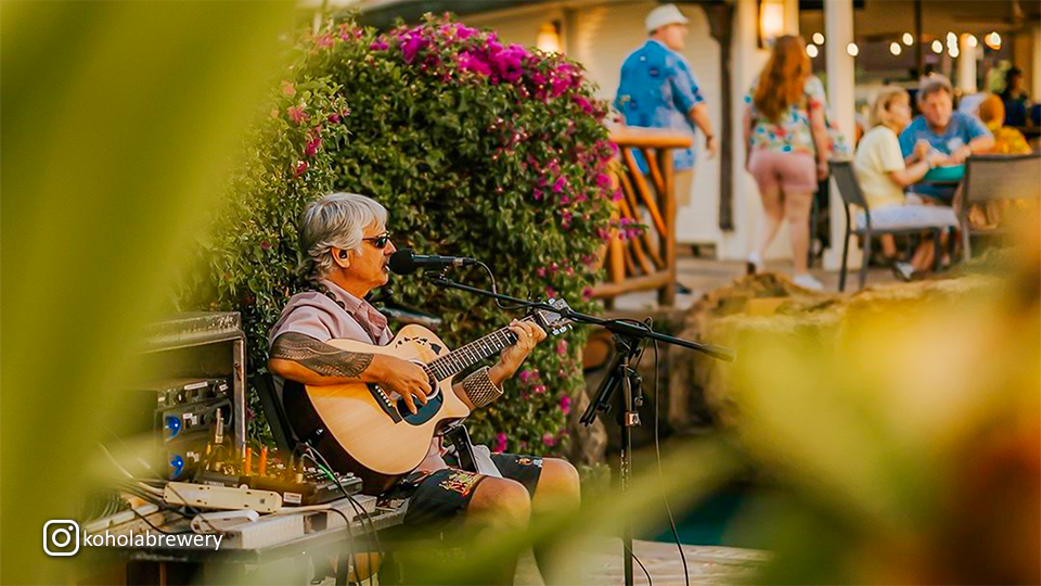 Guitarist performing at Kohola Brewery’s Tap Room outdoor area, captured in an artistic shot.