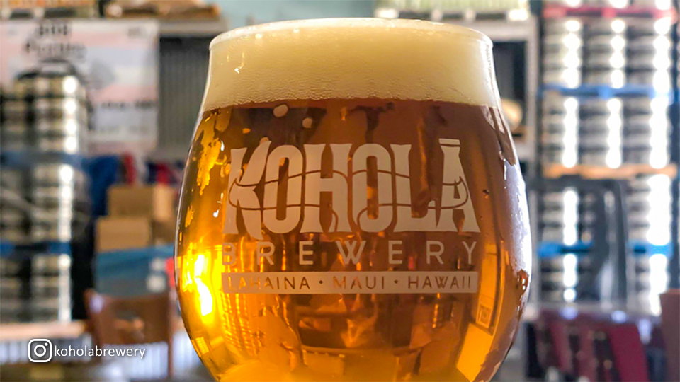 Close-up of a beer glass with the Kohola Brewery logo, with a blurred background creating a focus on the drink.