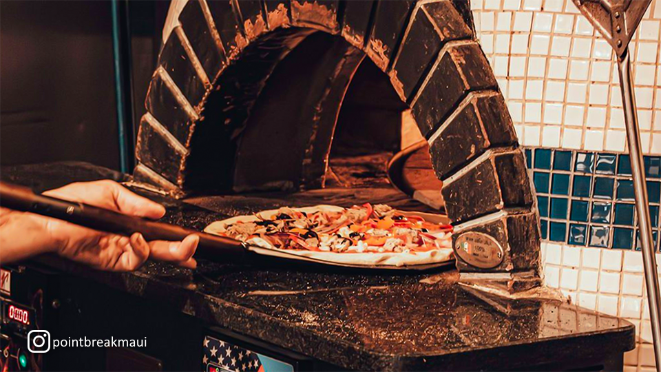 Pizza being placed into a wood-fired oven at Point Break Pizza & Panini, showcasing the authentic cooking process.