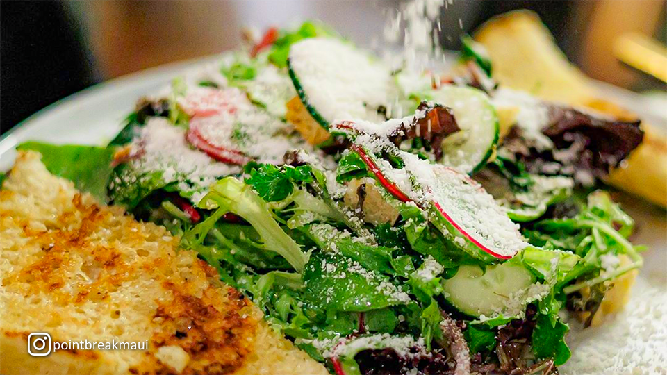 Close-up of a fresh salad with mixed greens, vegetables, and a piece of toasted bread served on the side.