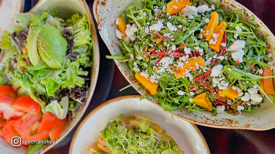 Overhead view of various salad dishes at Spoon & Key Market, showcasing fresh vegetables and vibrant toppings.