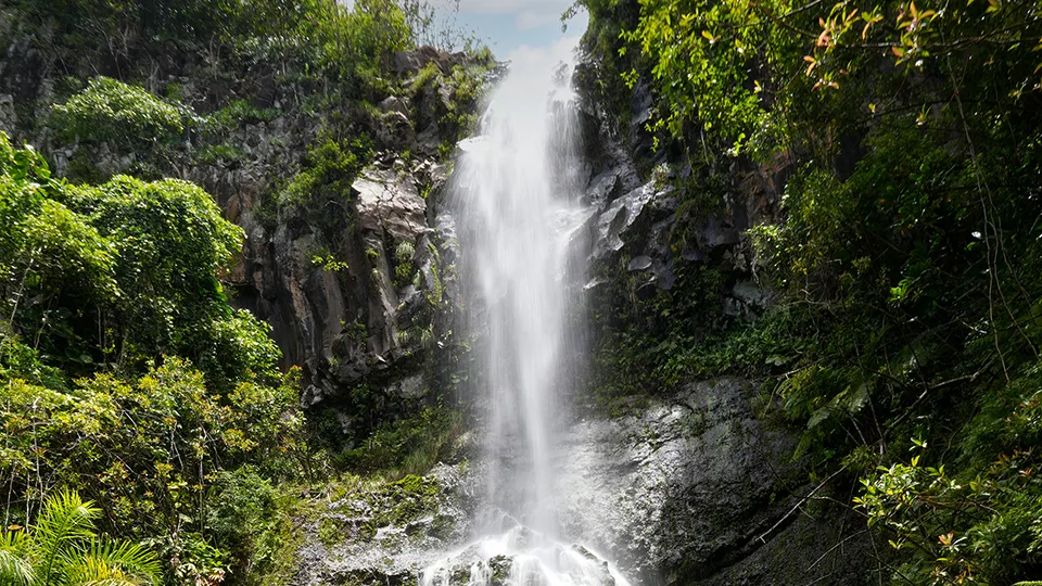 Wailua Falls cascading over volcanic rock formation with swimming pool at base Road to Hana